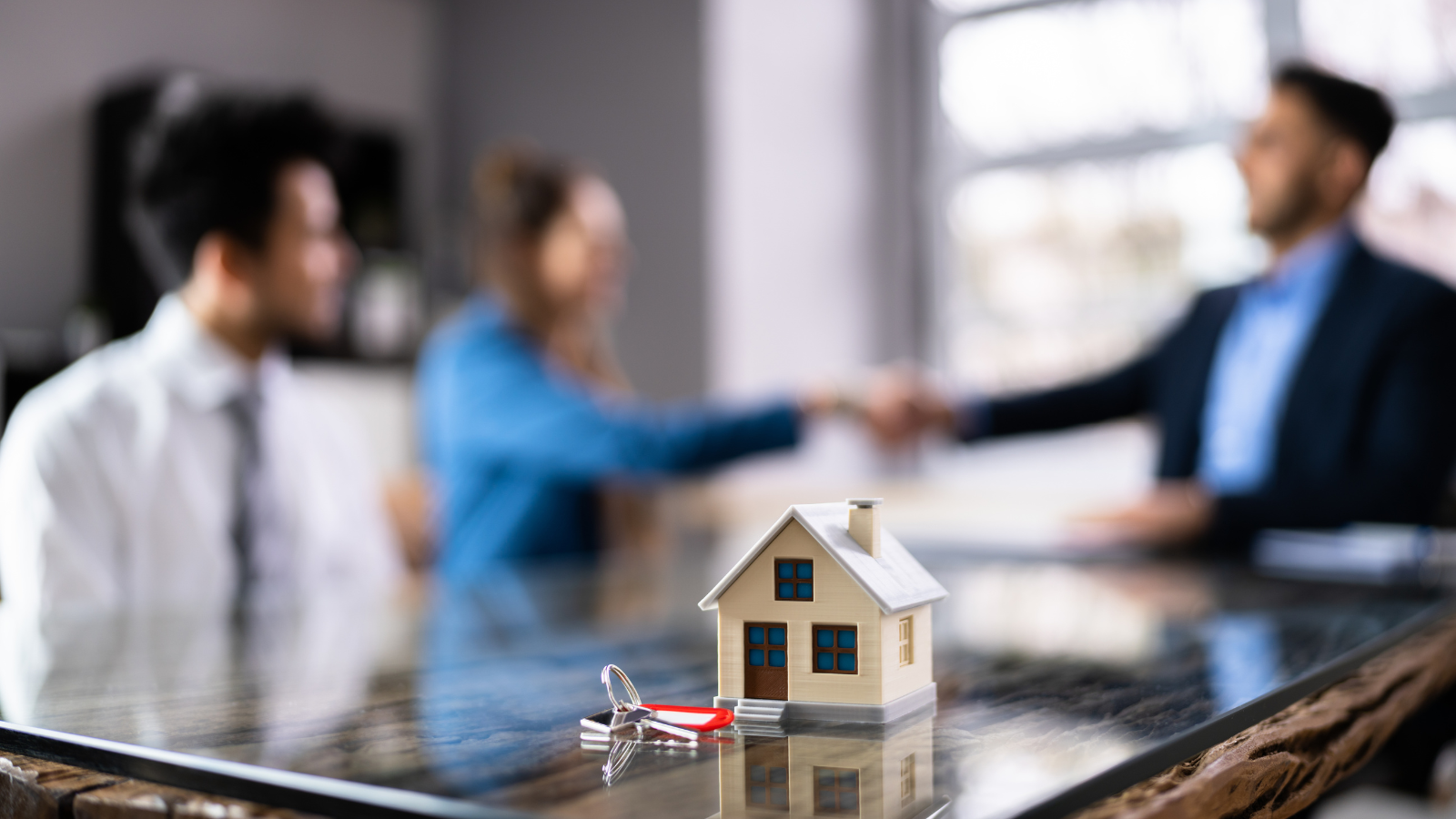 Couple shaking hands with mortgage broker over house model and keys - Salem Oregon home refinance closing consultation
