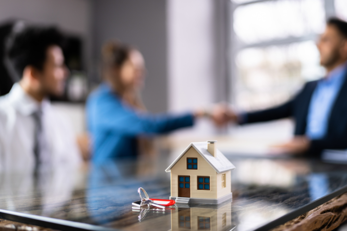 Couple shaking hands with mortgage broker over house model and keys - Salem Oregon home refinance closing consultation